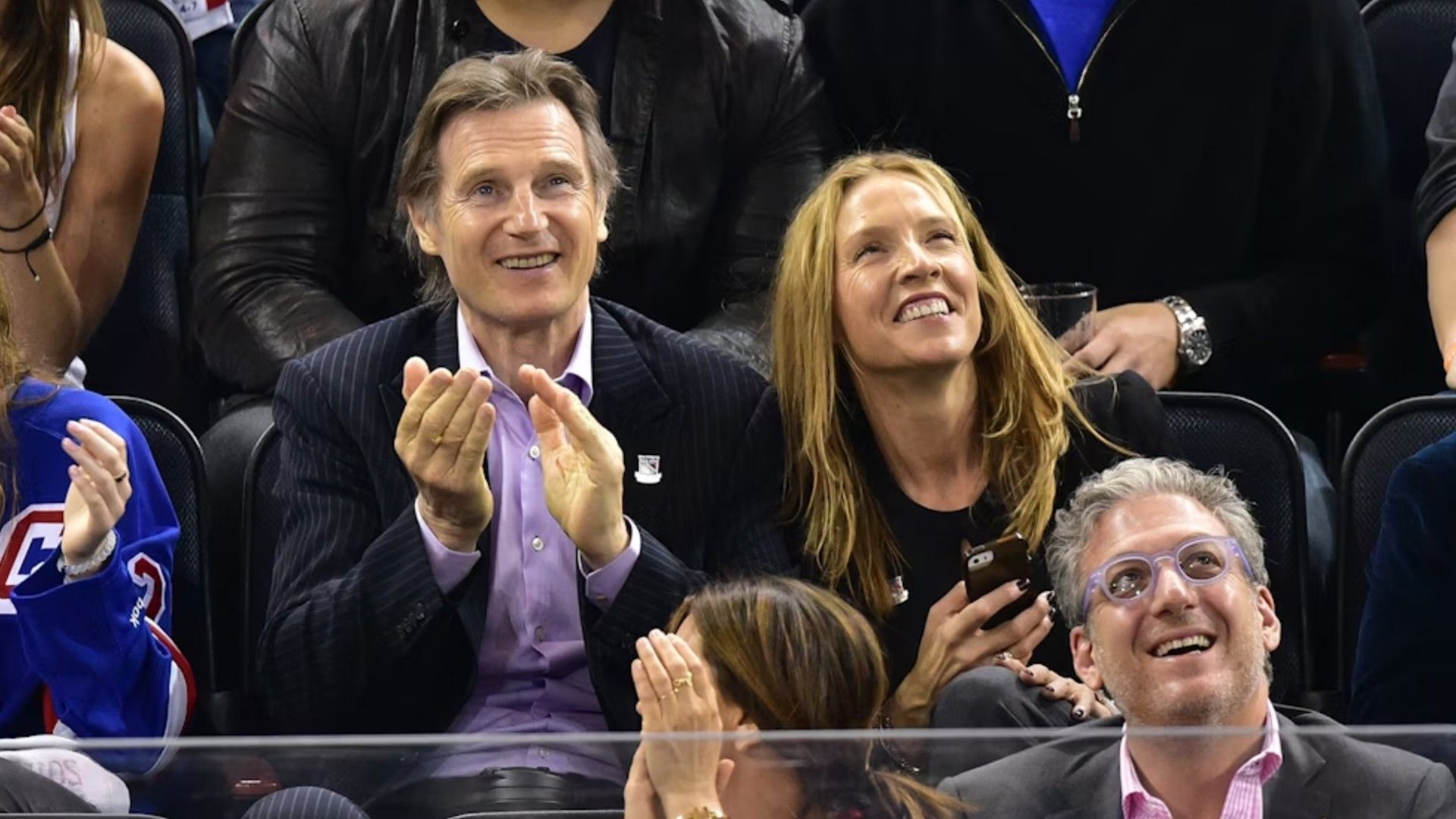 Liam Neeson and Freya St. Johnston sit in the stands during a sports match and cheer with joy