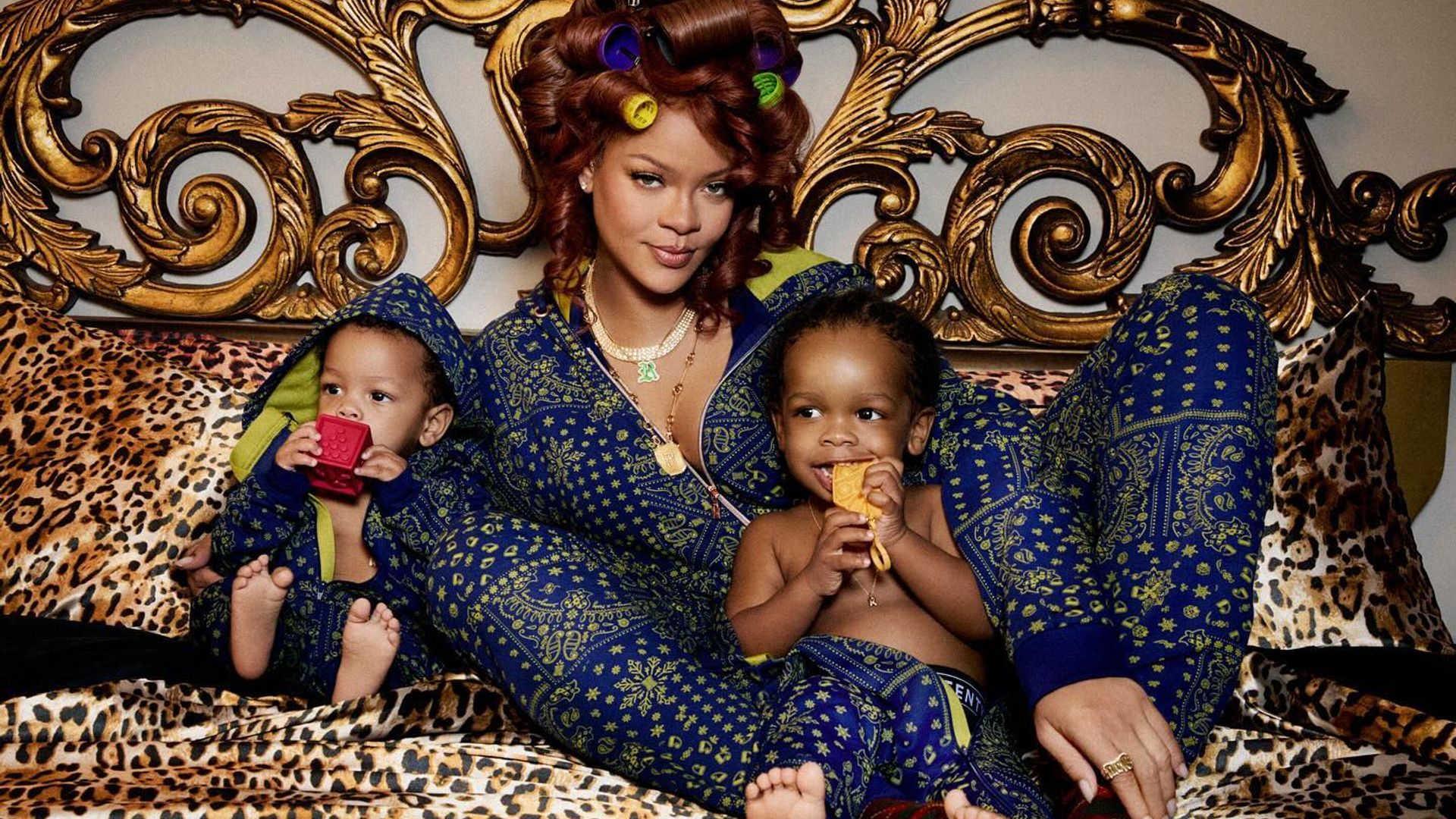 Rihanna in silk pajamas lying on a bed embracing her sons, photo shoot frame