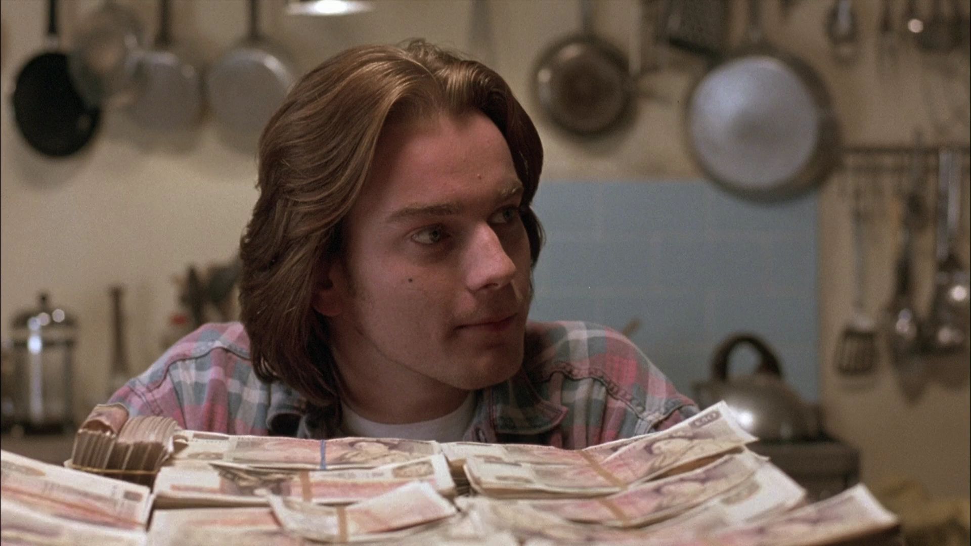 Young Ewan McGregor with long hair looking at a stack of money