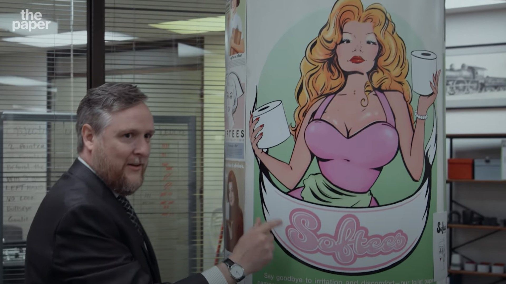 A man in a suit by a poster with a drawn blonde woman holding toilet paper rolls