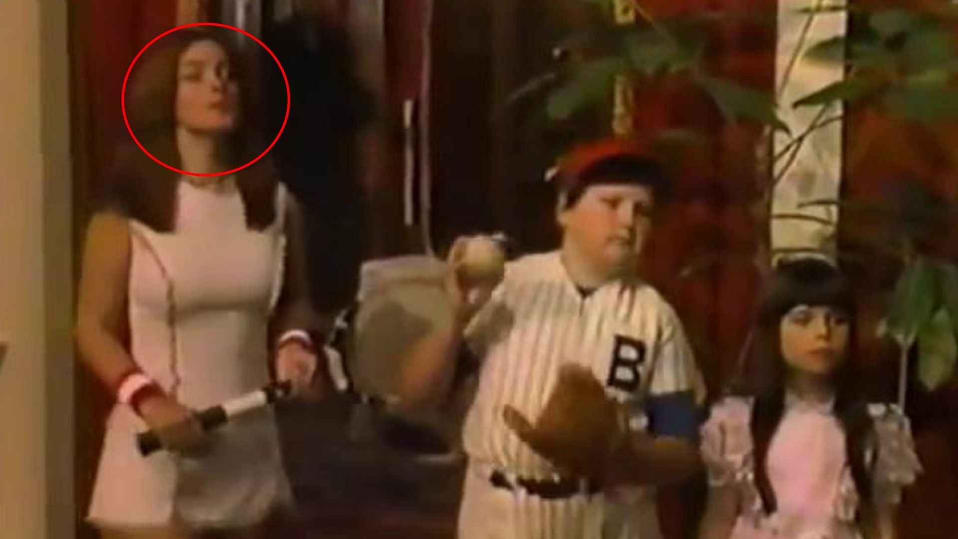 Woman in white tennis outfit with racket and two children in baseball and pink clothing indoors
