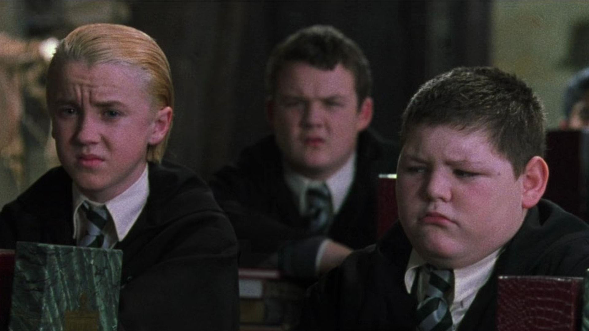Actor Tom Felton in school uniform sits next to two boys