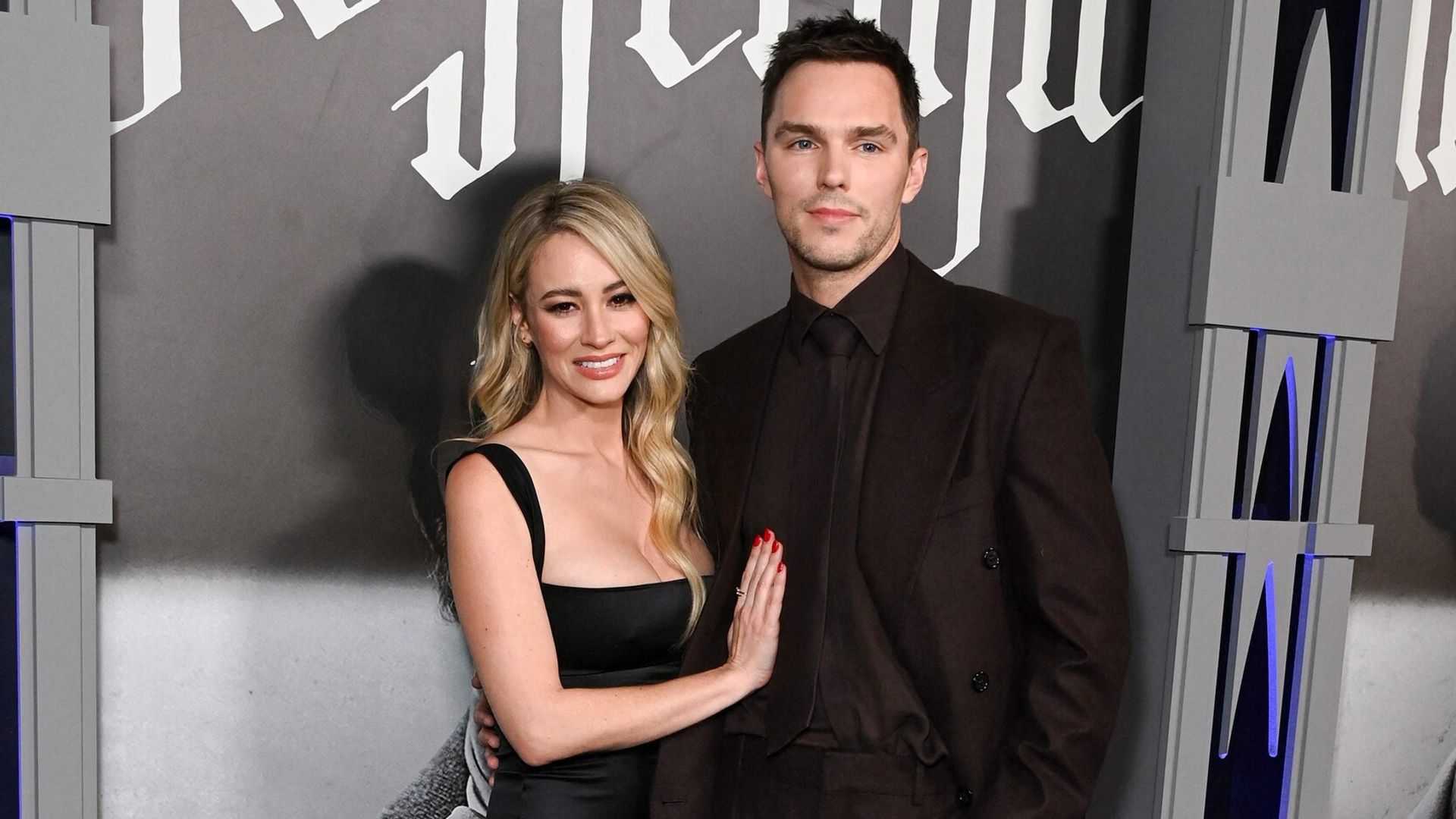Nicholas Hoult in a dark suit and Bryana Holly in a black dress pose together on the red carpet