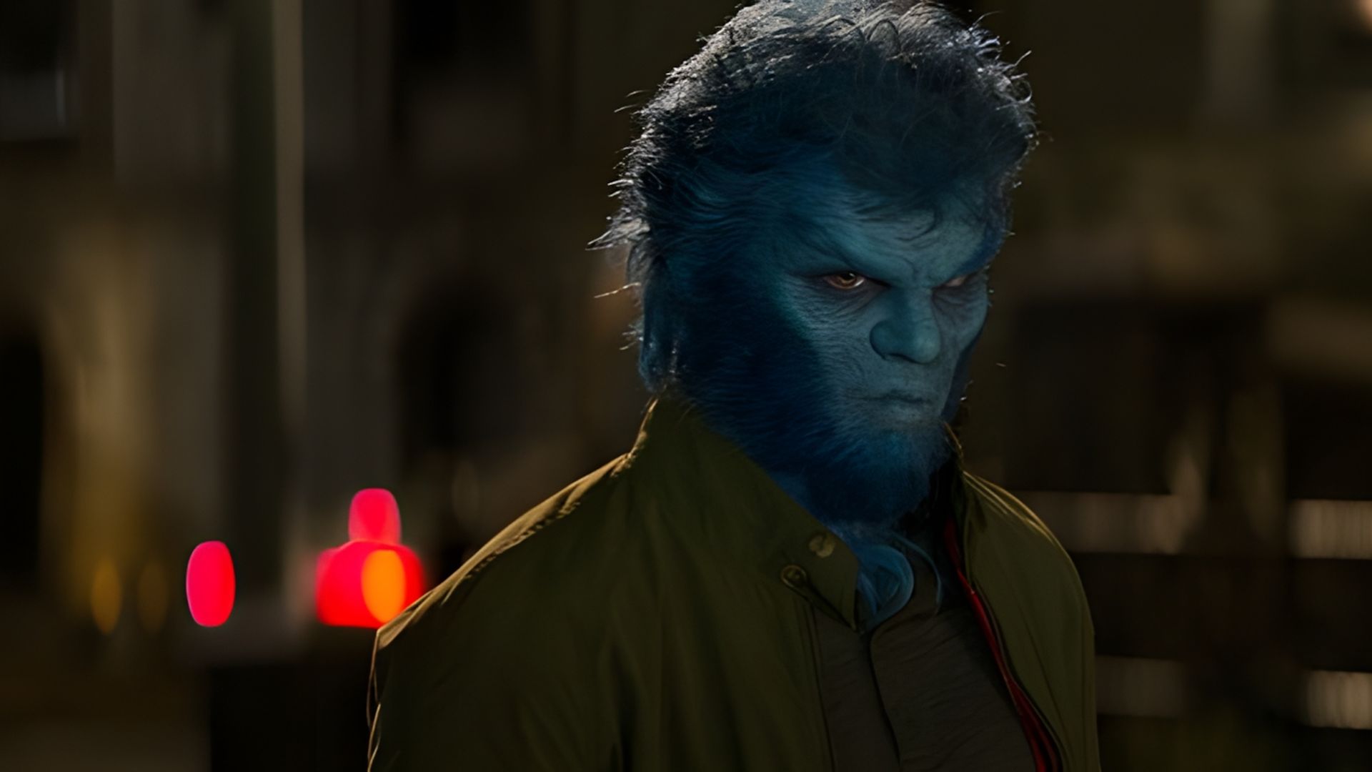 Nicholas Hoult with a blue face and fur in a green jacket stands at night on a dark street