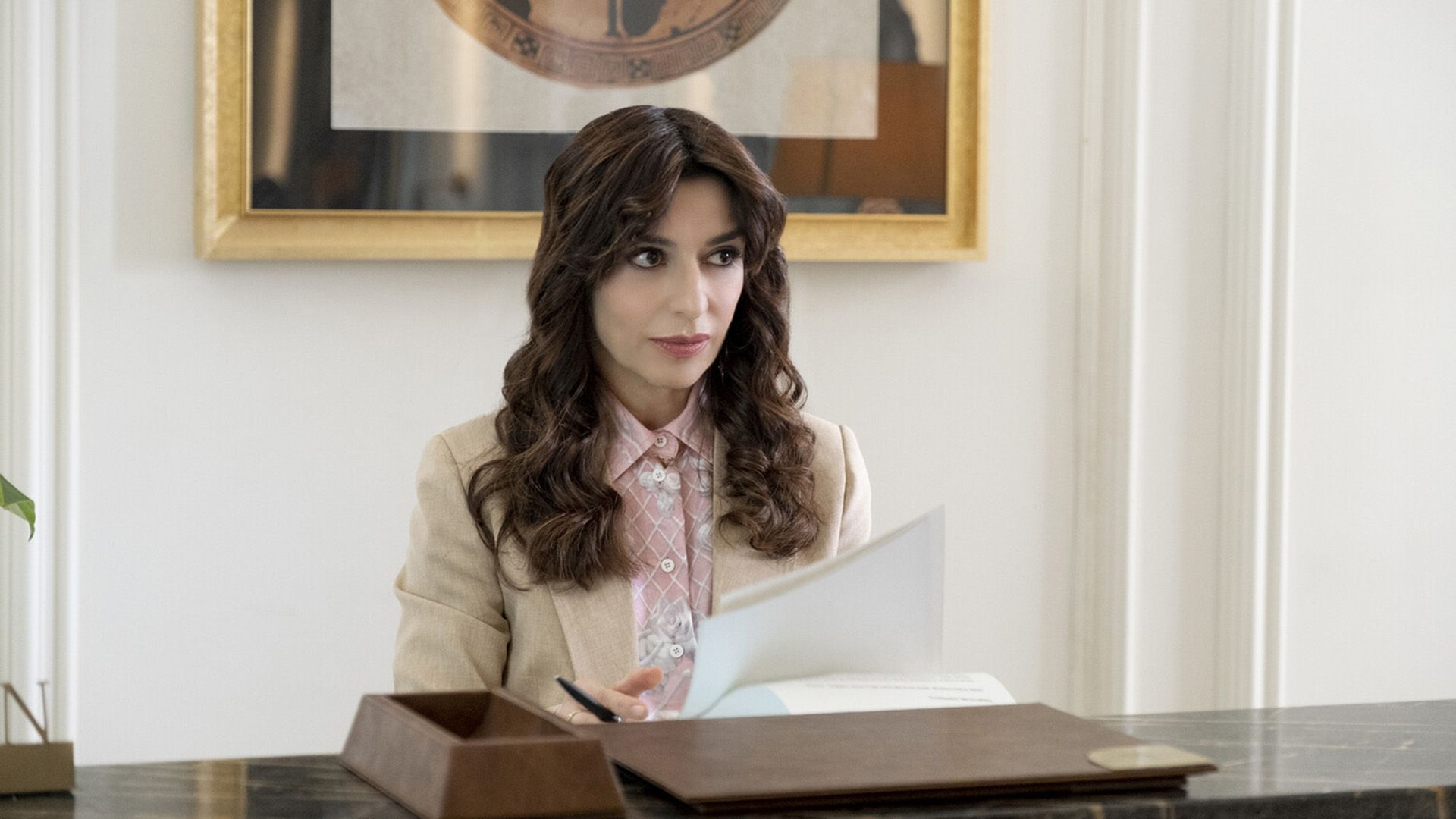 Sabrina Impacciatore in a beige blazer holding a pen and paper