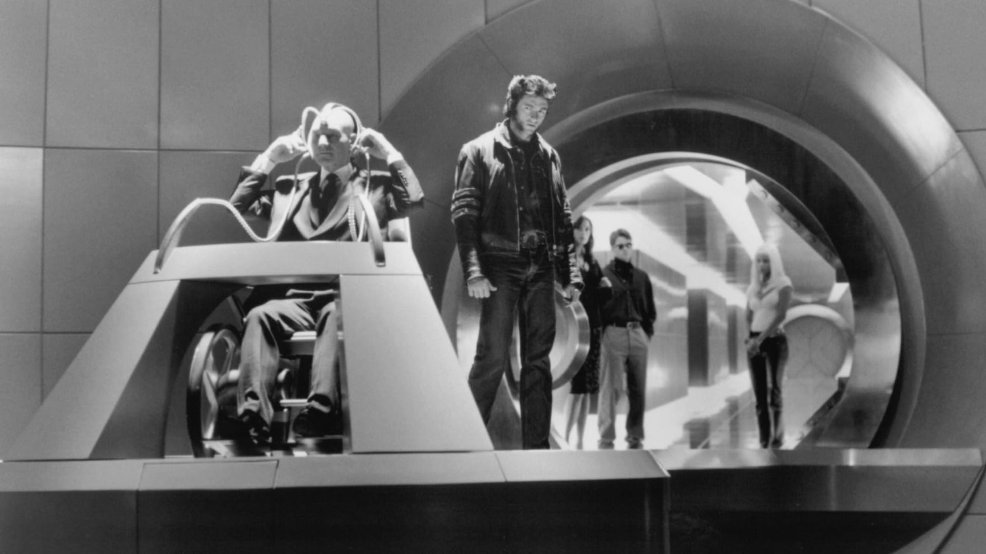 Actor Hugh Jackman in a leather jacket stands surrounded by people in a metal room
