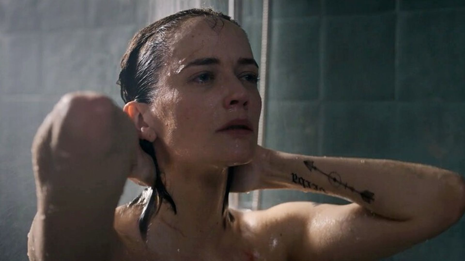 Eva Green with wet hair taking a shower, hands behind her head, only her face and tattooed arm visible