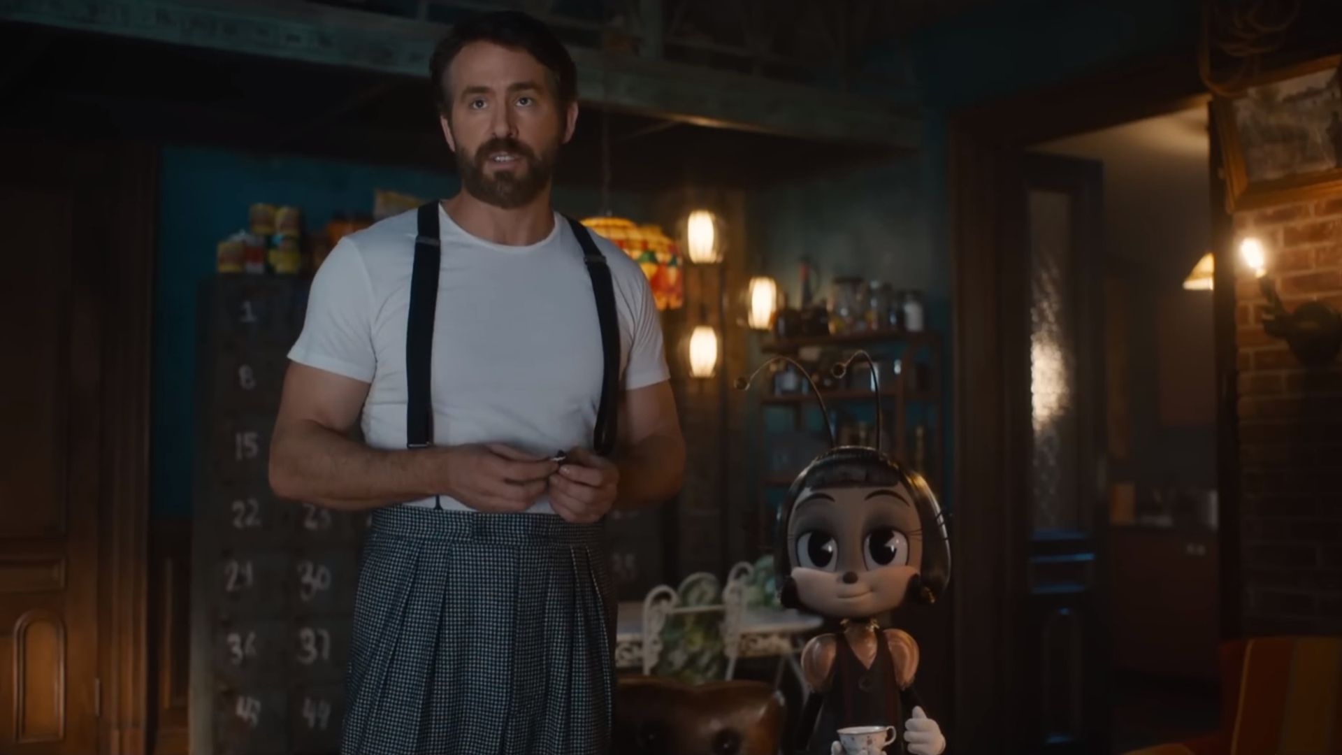 Ryan Reynolds in a white t-shirt with suspenders stands next to a cartoon ant character holding a cup of tea