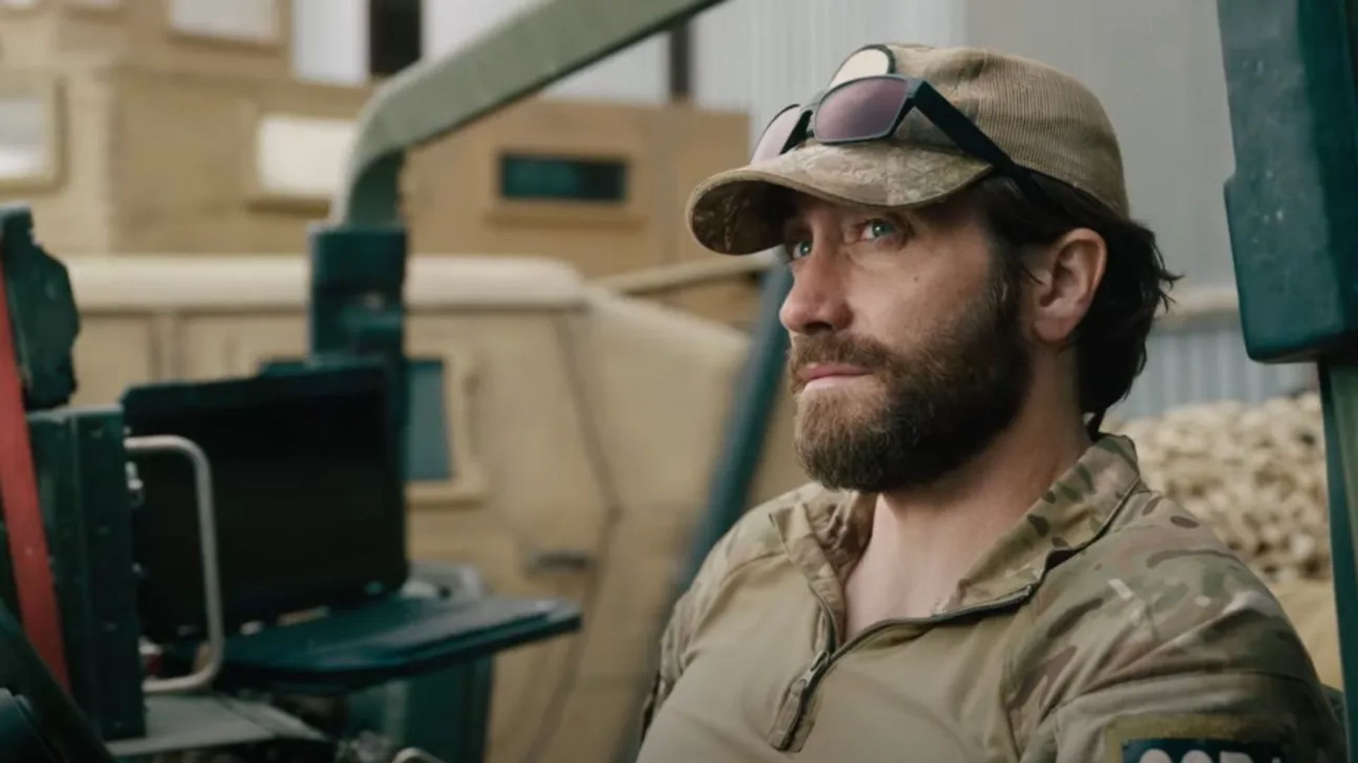 Jake Gyllenhaal in military uniform and cap with glasses on the visor sits looking to the side with a serious expression
