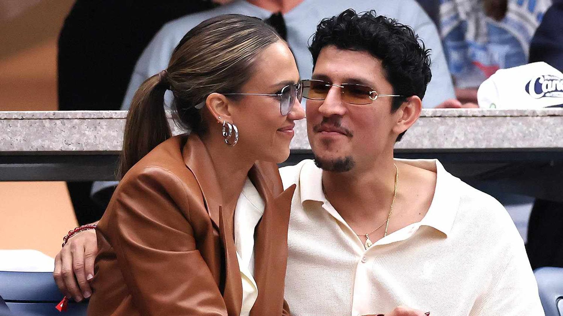 Jessica Alba and Danny Ramirez sitting in the stands at a sporting event embracing each other