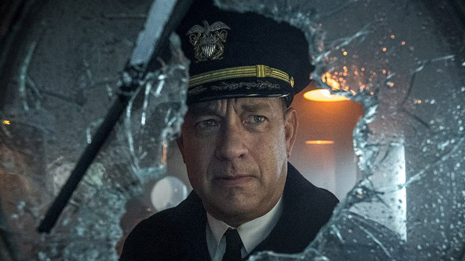 Tom Hanks in captain's uniform looks through broken glass with a serious expression on his face