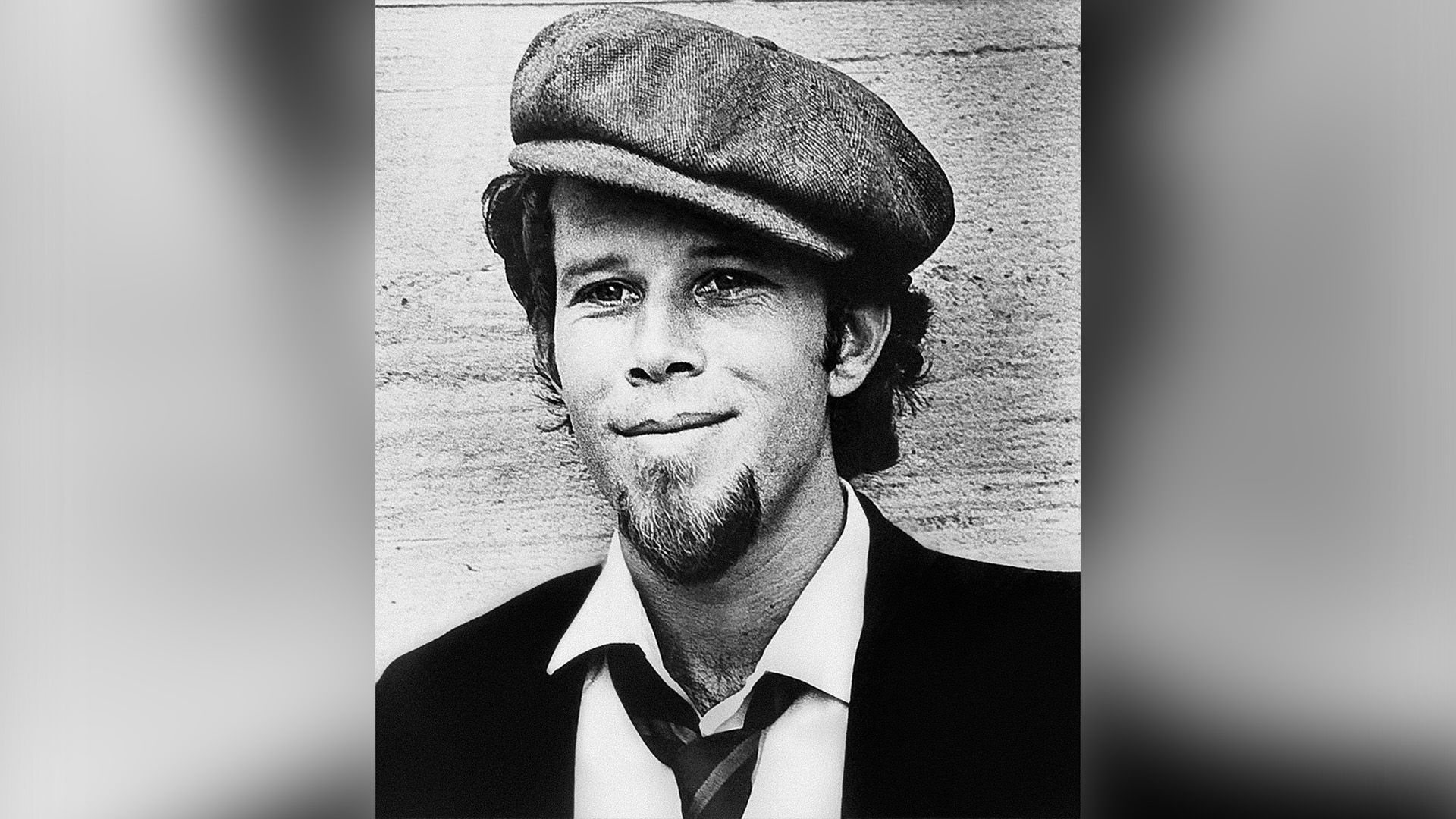 Young Tom Waits in a cap smiling