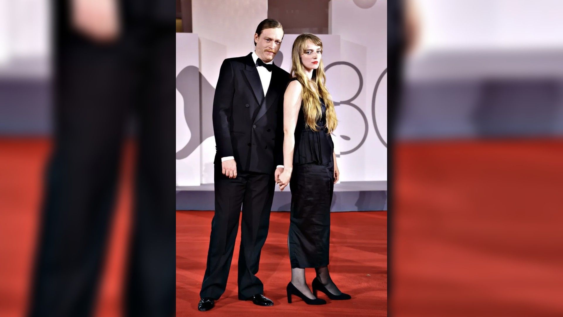Caleb Landry Jones and Katya Zvereva in evening attire pose on the red carpet, holding hands