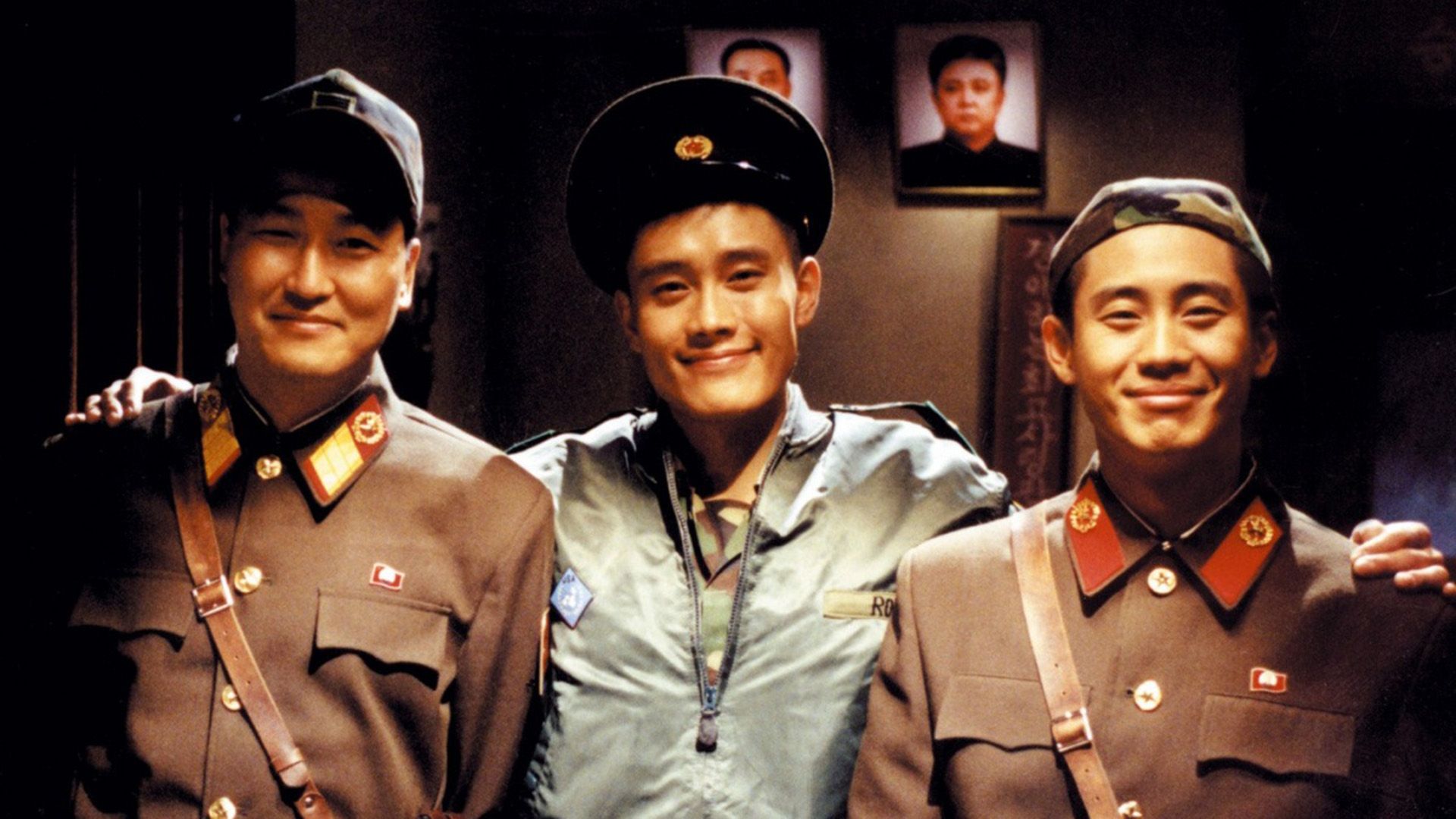 Lee Byung-hun has his arms around the shoulders of two men in military uniforms, all three are smiling