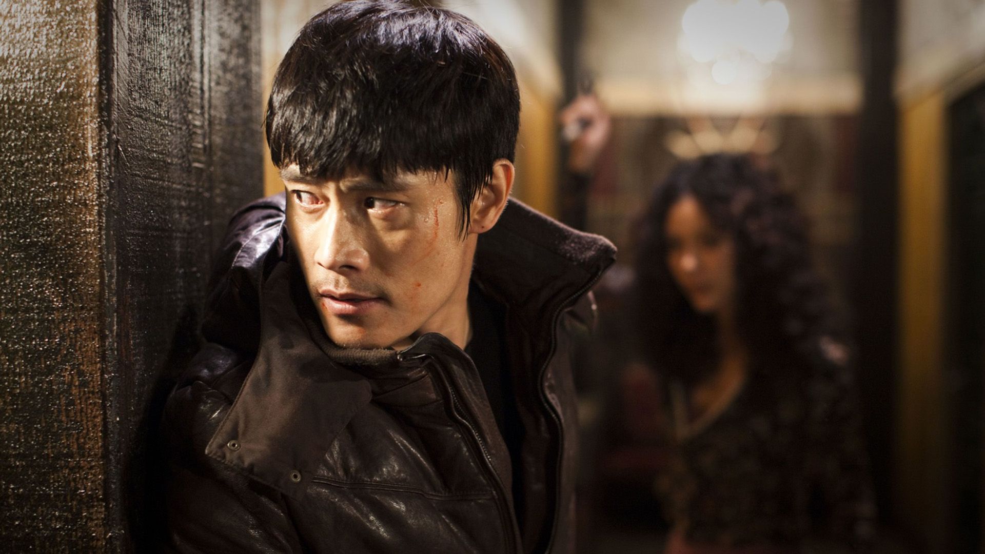 Lee Byung-hun in a black jacket peeks around the corner of a building