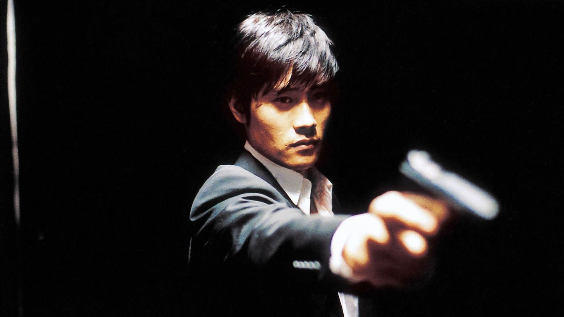 Lee Byung-hun in a white shirt and jacket holds a gun in his outstretched hand