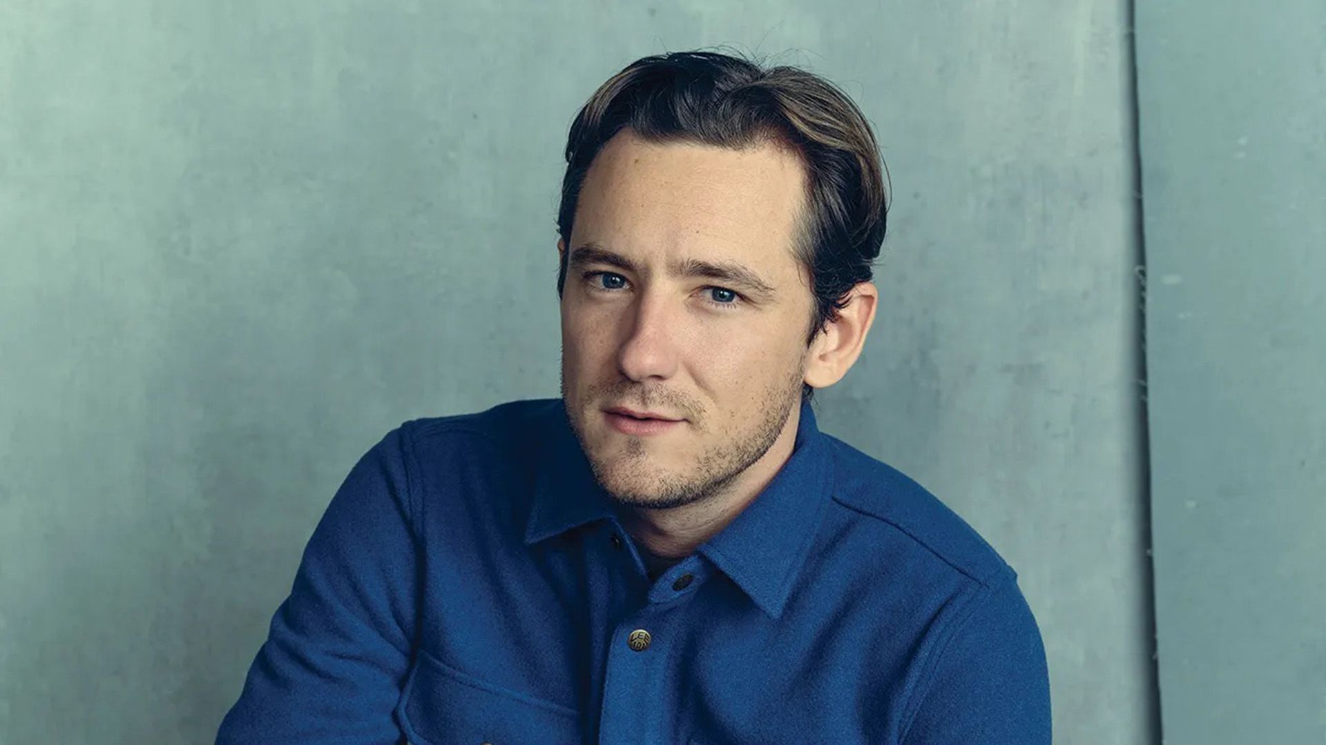 Actor Lewis Pullman in a blue shirt against a light blue background