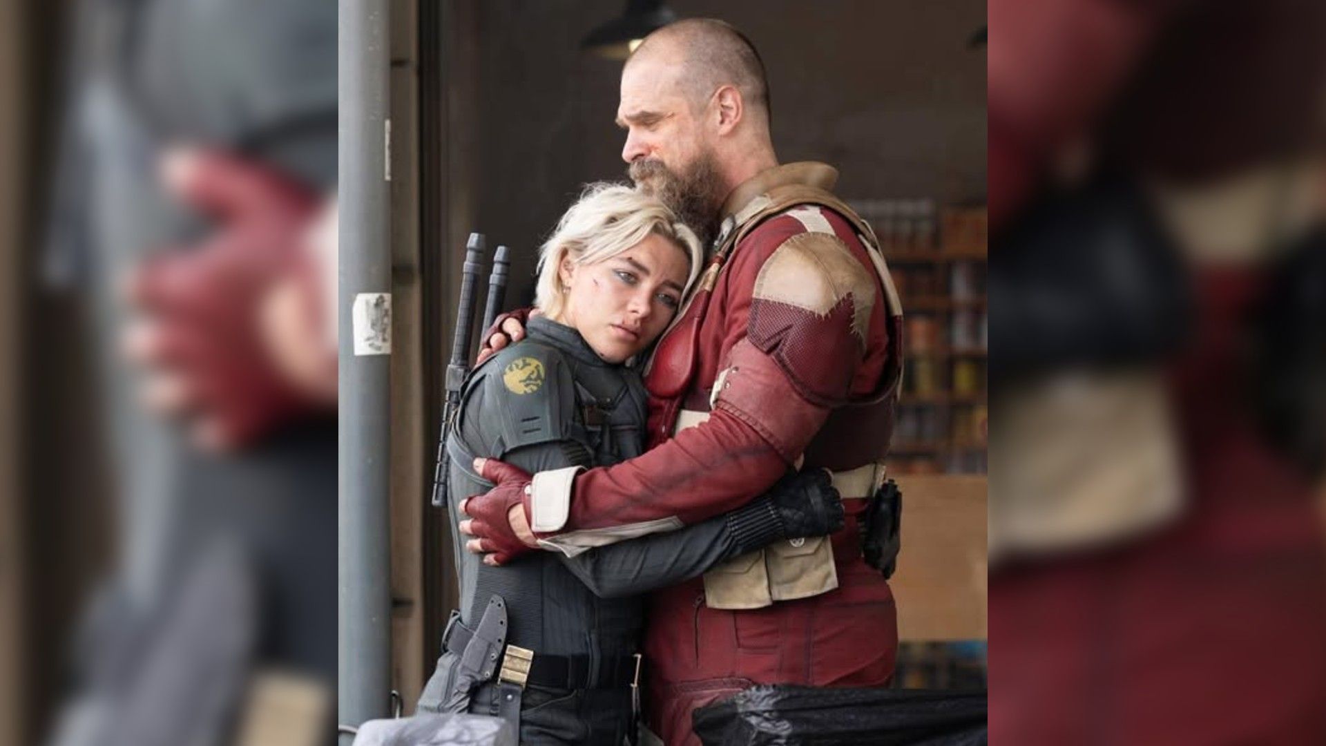 David Harbour and Florence Pugh in superhero costumes embracing, profile view