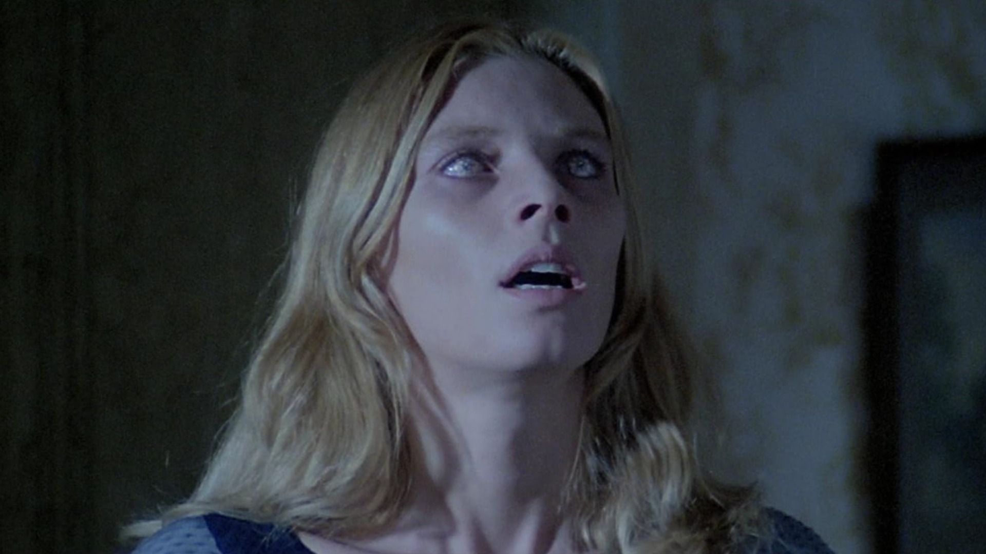 A girl with completely white eyes opened her mouth against a gray wall background