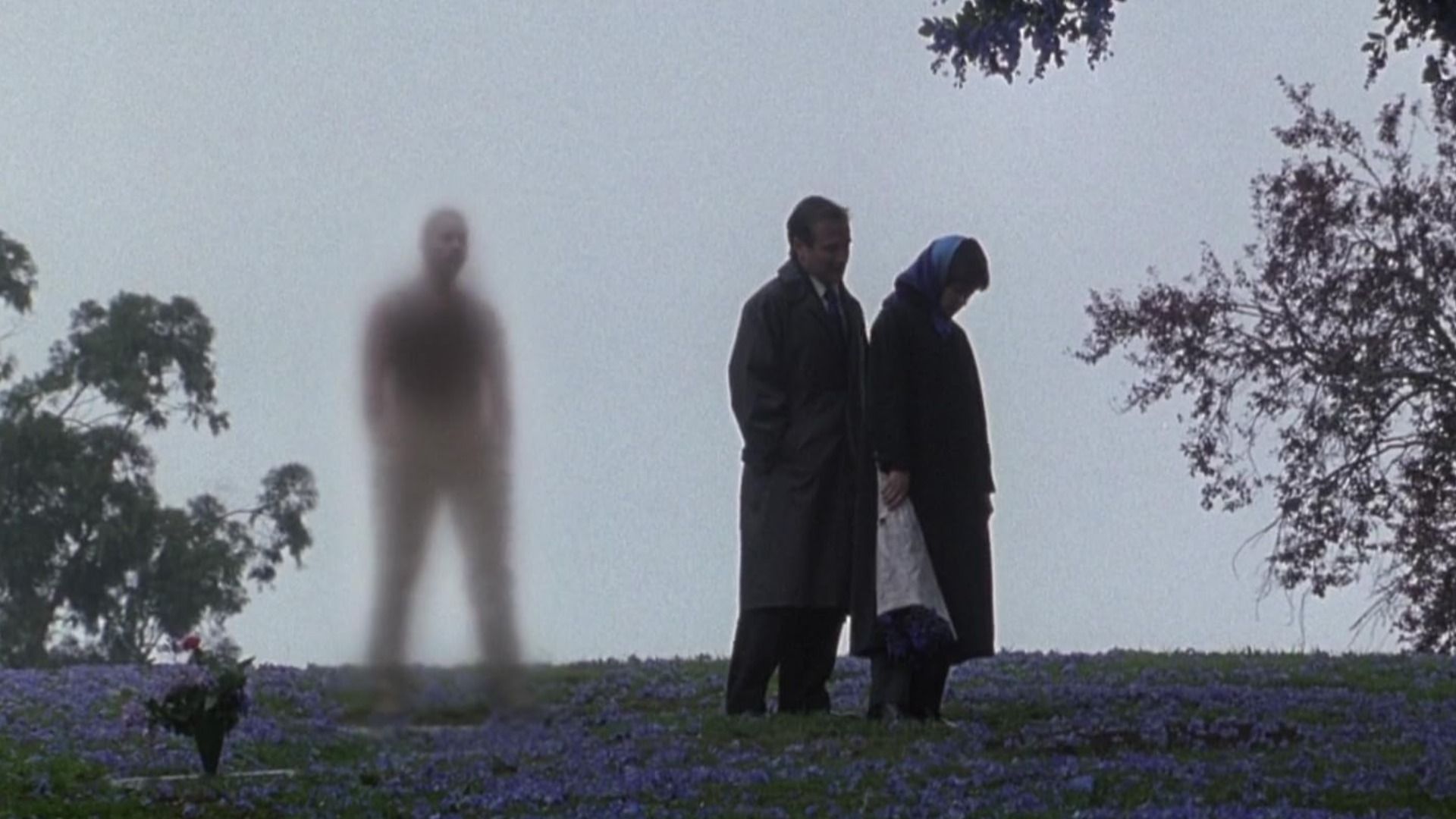 A man and woman stand by a tree with a blurry human figure beside them