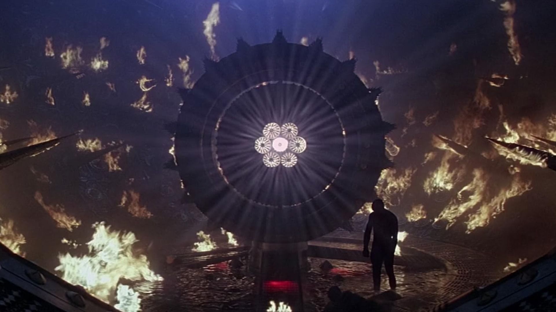 A man stands by a round iron structure surrounded by flames