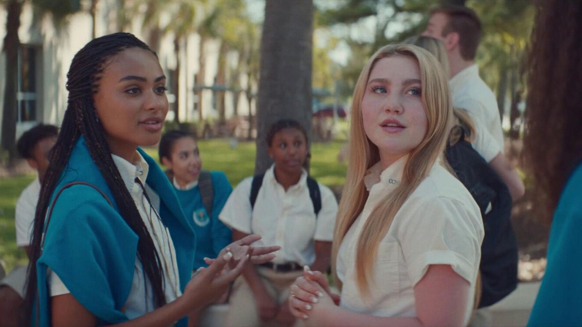Ella Anderson and Nico Parker talking while standing against a backdrop of palm trees