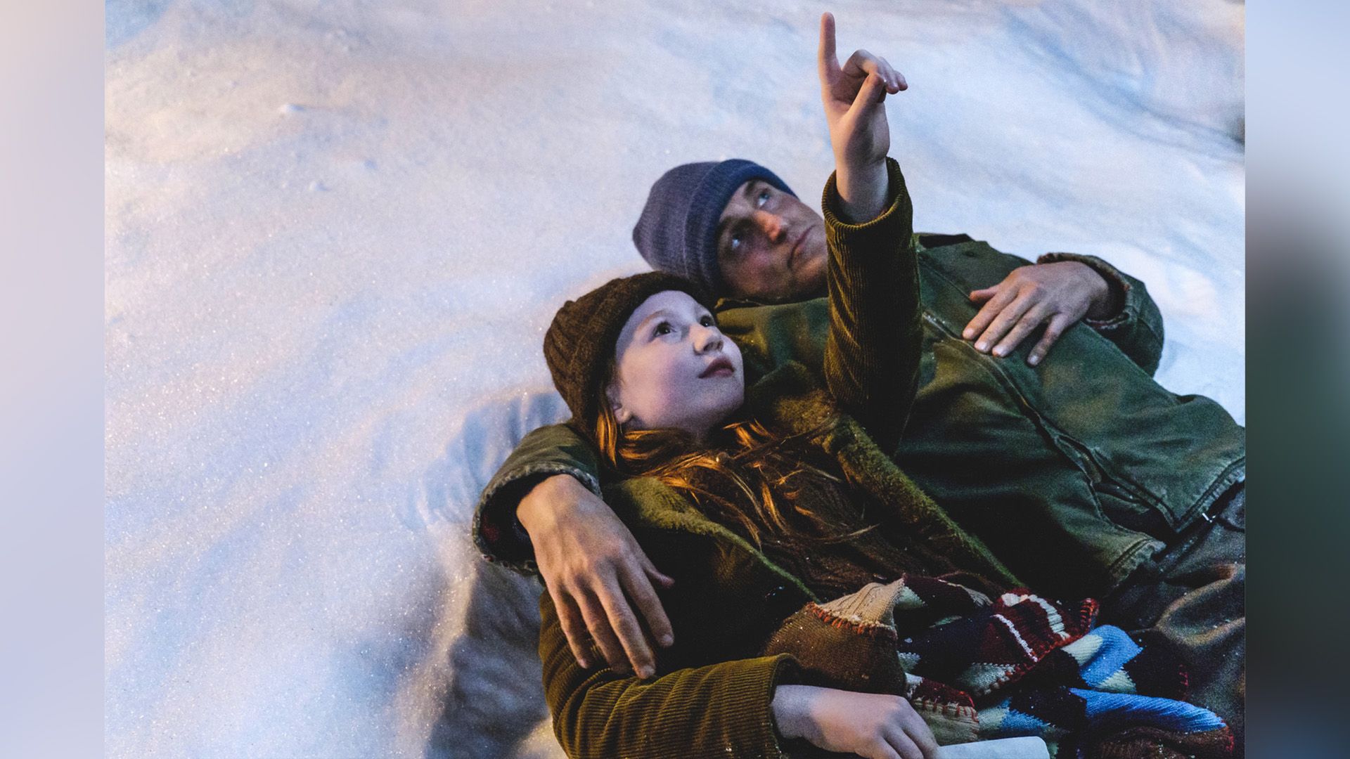 Ella Anderson and Woody Harrelson are lying in the snow with Ella pointing up at the sky