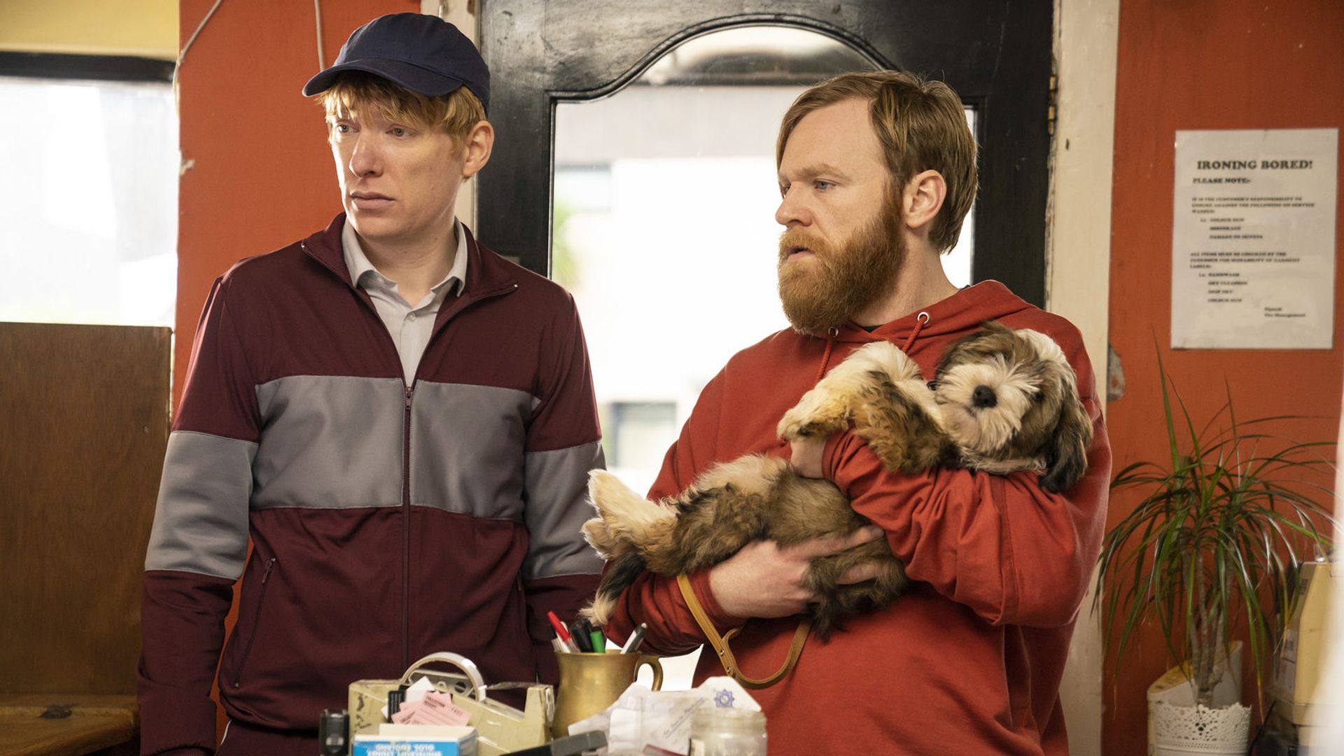 Brian and Domhnall Gleeson in sportswear standing by a table looking to the side