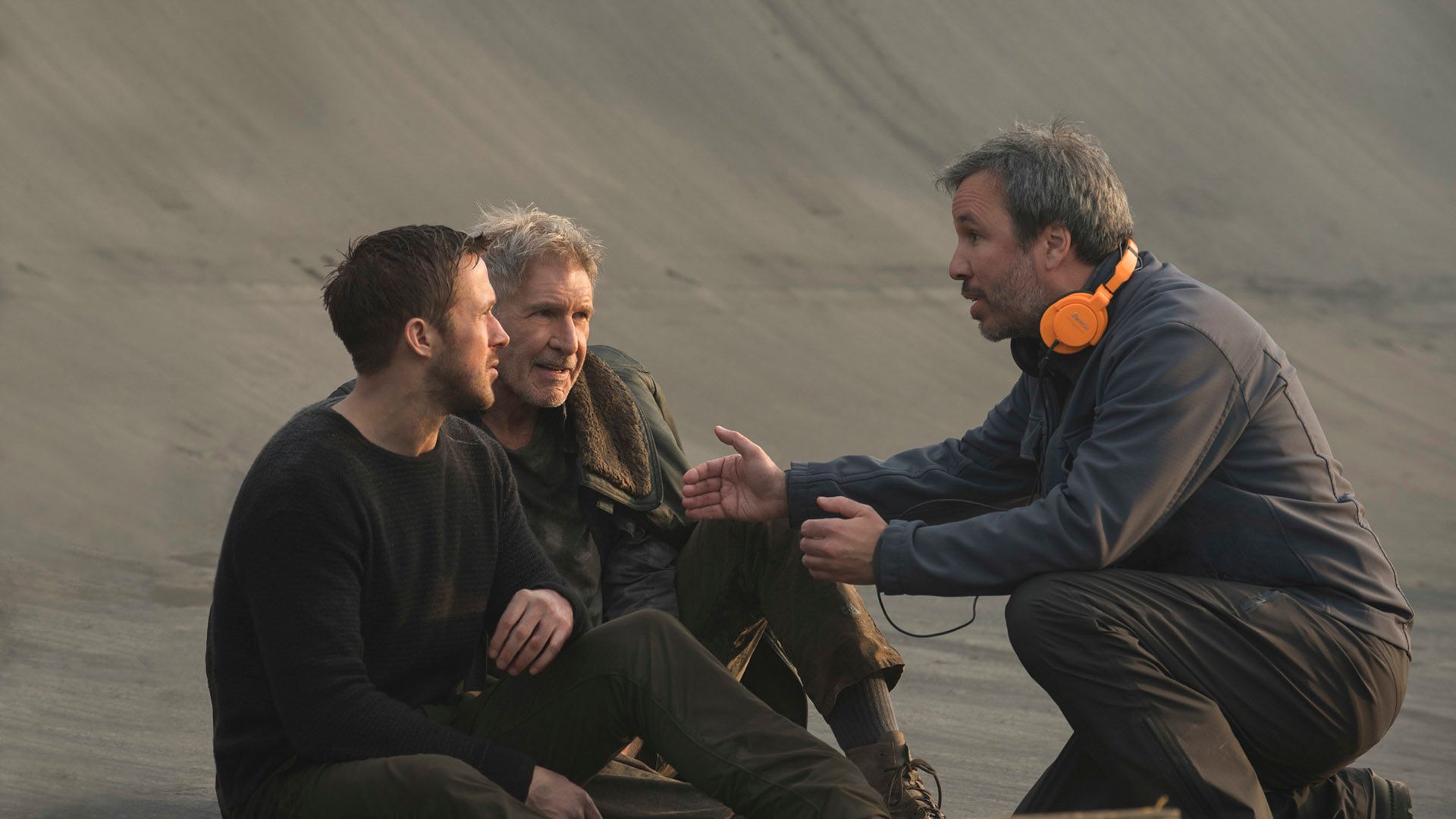 Denis Villeneuve, gesticulating, explains something to Ryan Gosling and Harrison Ford sitting in front of him