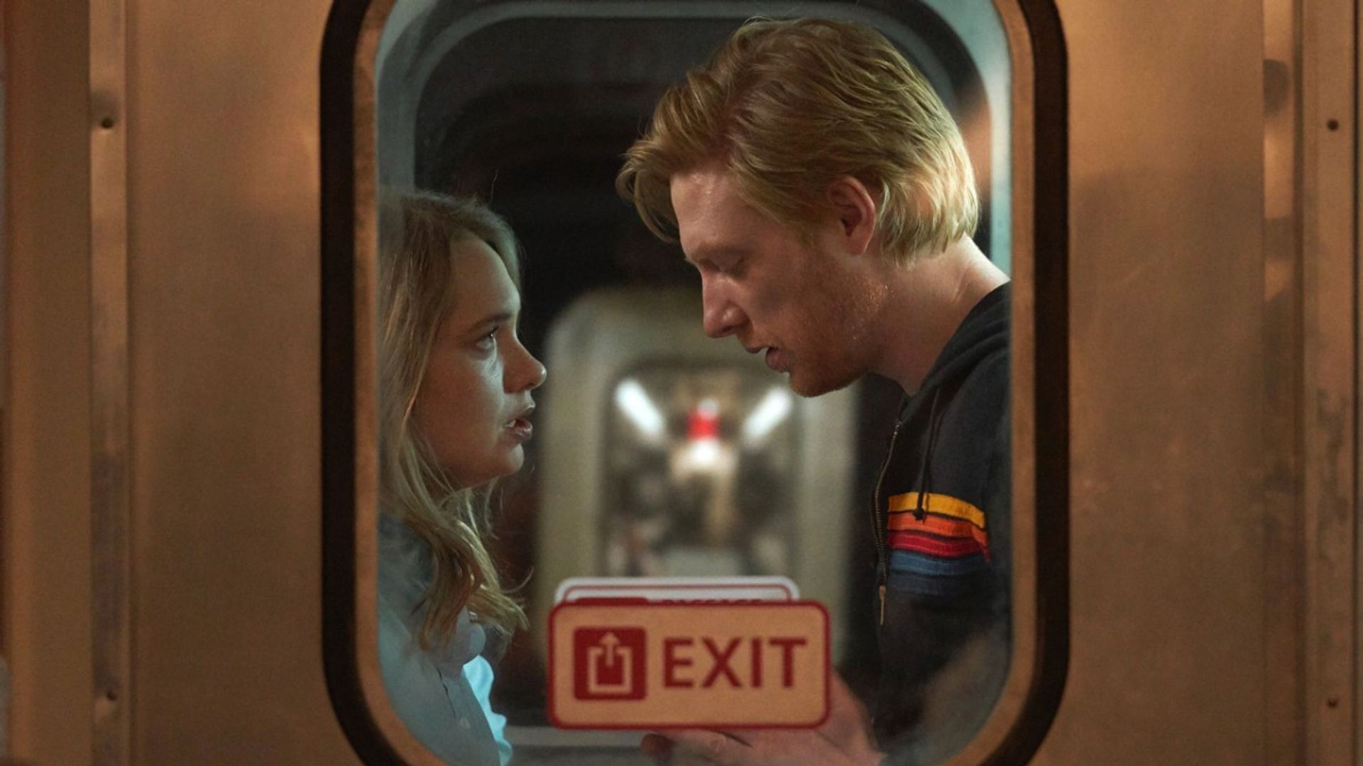 Domhnall Gleeson and Merritt Wever stand face-to-face in a train vestibule, shot from outside the window