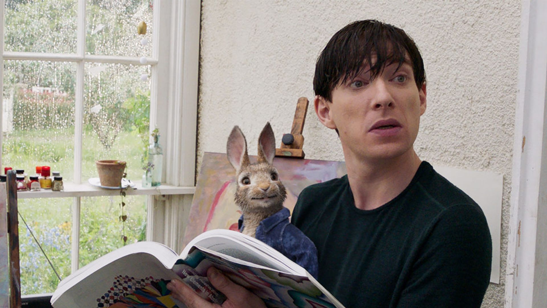 Domhnall Gleeson sits reading a newspaper with a toy rabbit on his lap