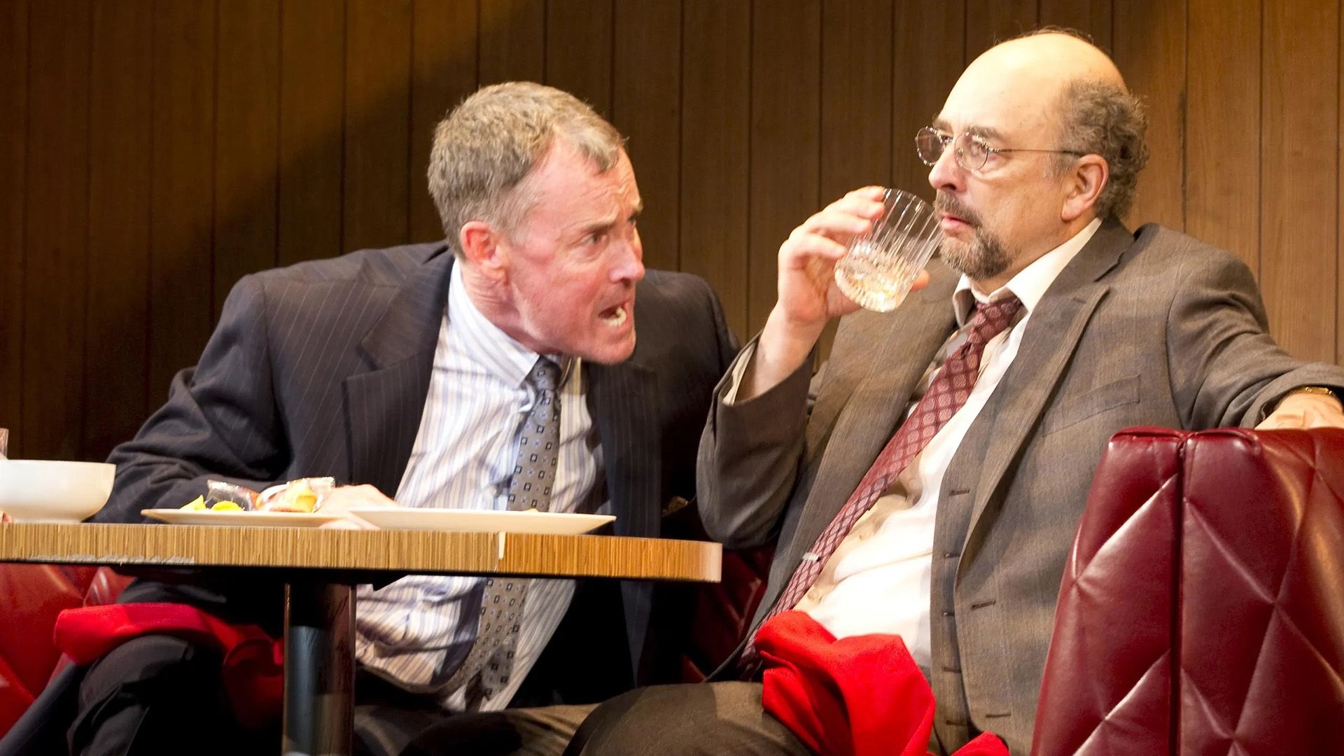 John C. McGinley sitting at a cafeteria table yelling at a man wearing glasses sitting next to him