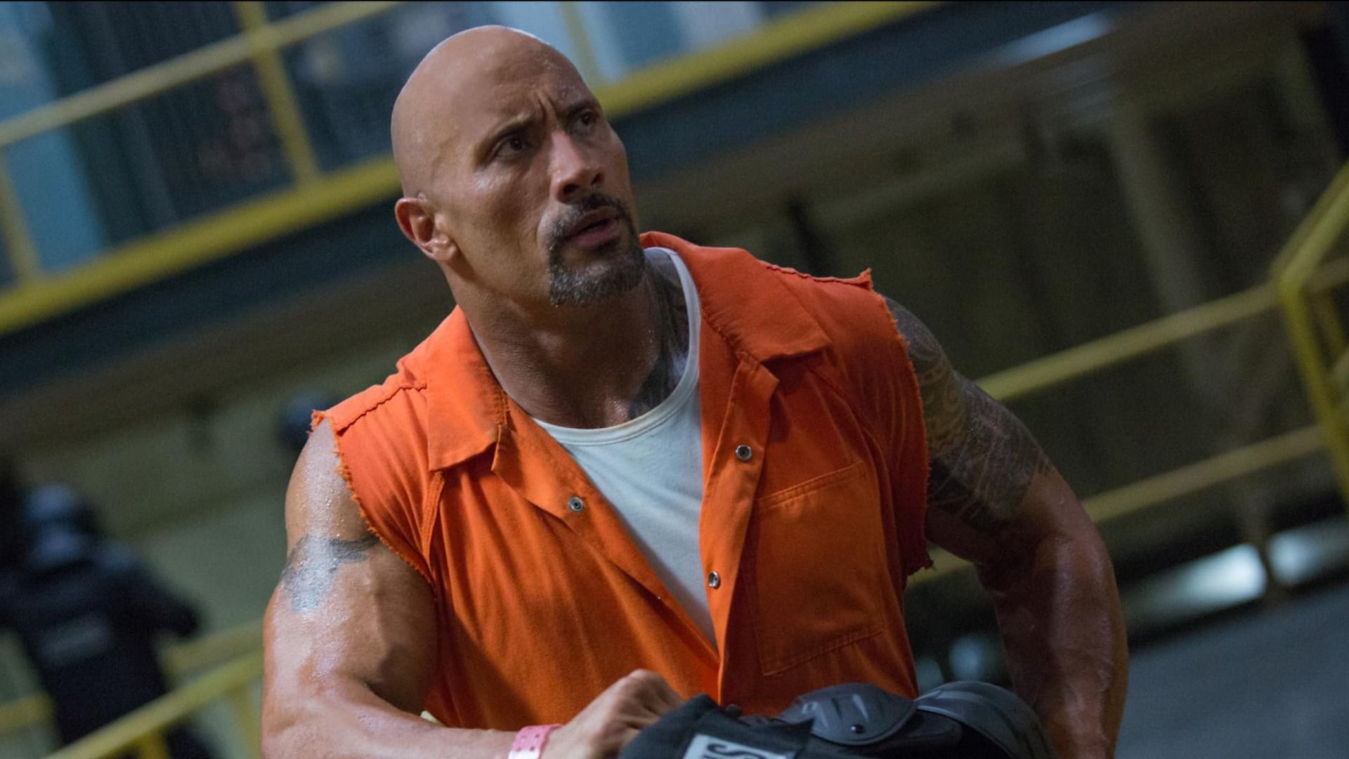 Actor Dwayne Johnson in an orange vest sits against a backdrop of prison cells